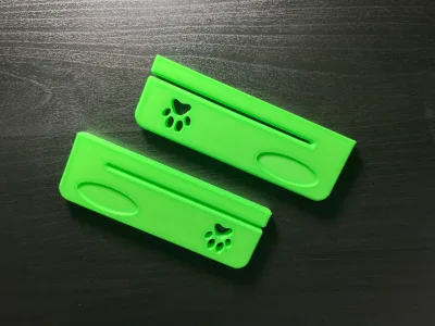 Two green squeezers side by side on a dark surface, the slot and the paw print visible
