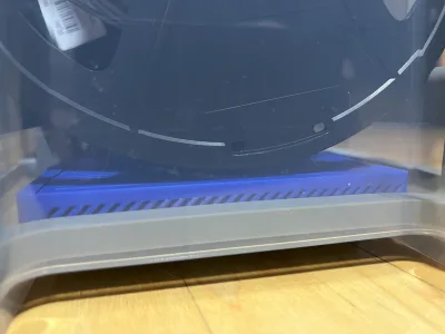 Blick von der Seite in die durchsichtige Kiste: die blaue Box liegt flach unter einer Filamentspule, ihre schräg gedruckten Lüftungsschlitze sind zu sehen