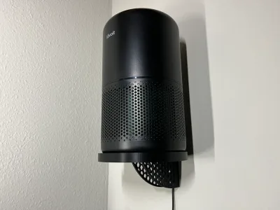 The black air purifier stands on the round wall shelf against a white wall